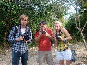 Two young men and a young women hold up their cameras