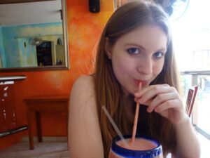 Young girl eyes the camera as she sips a pink smoothie from a straw