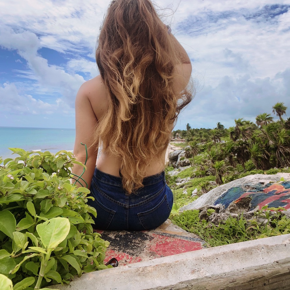 Girl with long hair sits on cliff over beach